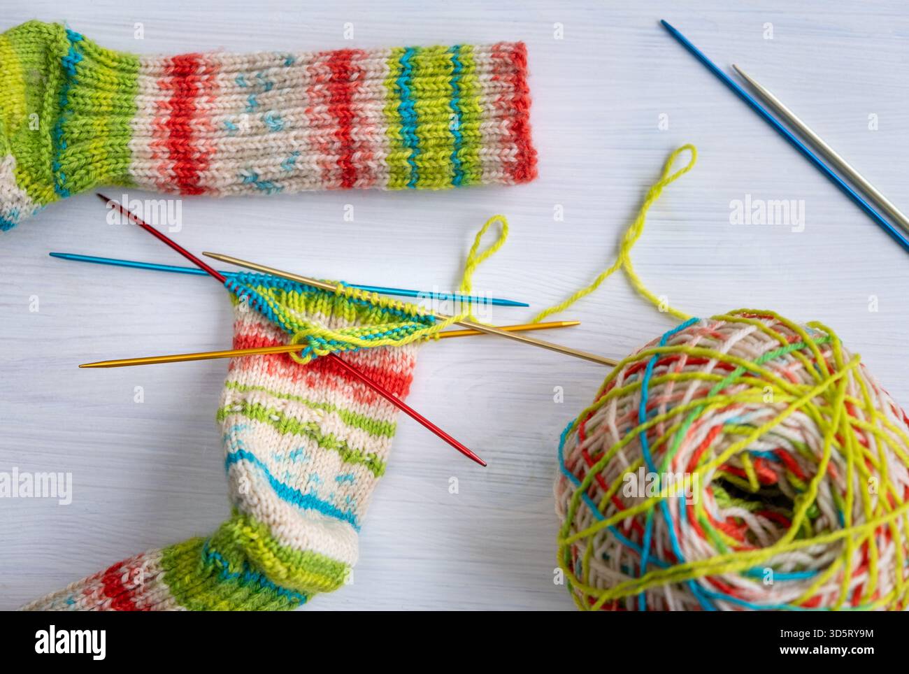 Vista dall'alto verso il basso di un progetto di maglieria calzini con filato di lana e aghi disposti insieme, che mostrano colori, texture e dettagli artigianali fatti a mano, ideali per Foto Stock