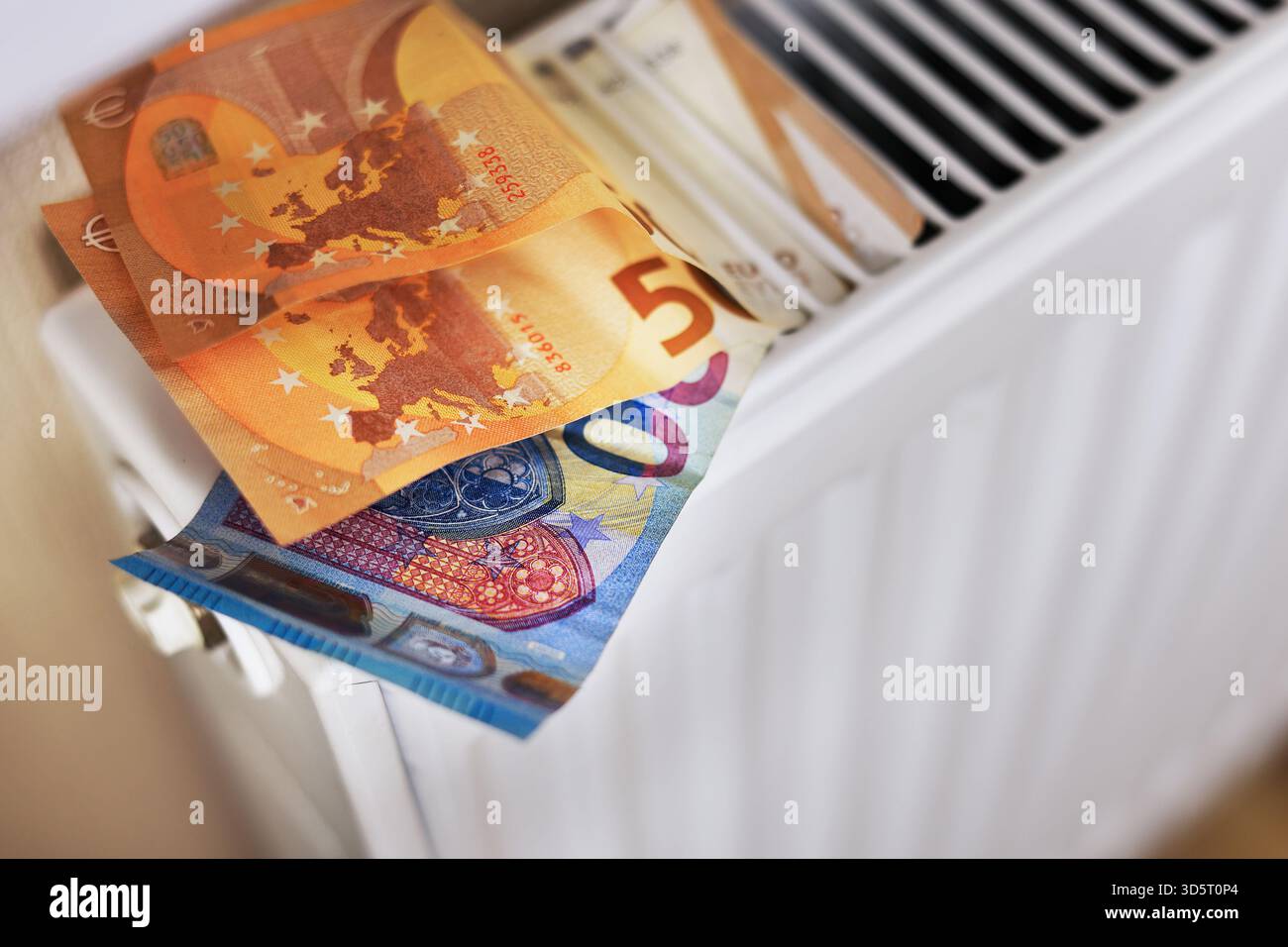 Un primo piano di un radiatore bianco con banconote da 15 e 20 euro, simbolo del periodo di elevate tariffe di riscaldamento. Foto Stock