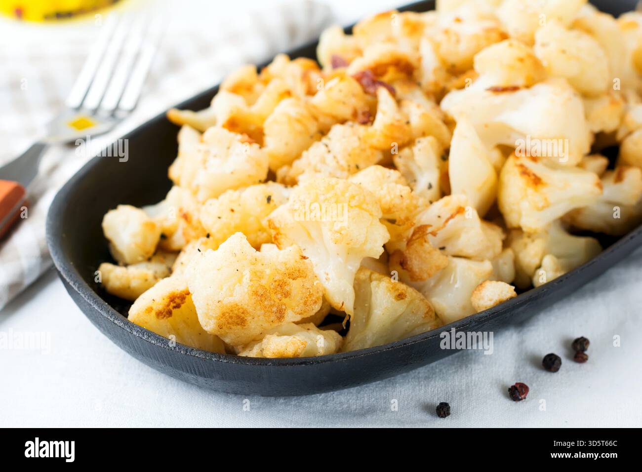 Cavolfiore al forno con spezie e aglio in una padella in ghisa su uno sfondo chiaro. Messa a fuoco selettiva. Foto Stock