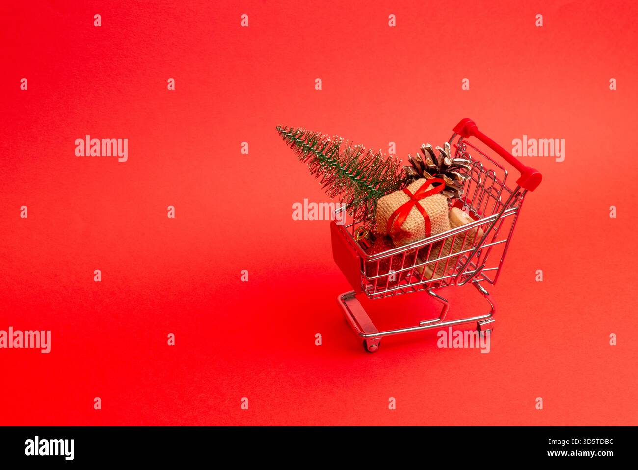 Mini cart con articoli da regalo avvolti e coni di pino su sfondo rosso brillante con ampio spazio per le copie Foto Stock