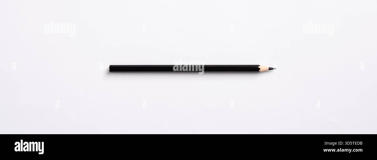 Primo piano minimalista di una matita nera appoggiata su una superficie bianca incontaminata, che enfatizza la semplicità e il potenziale di creatività Foto Stock