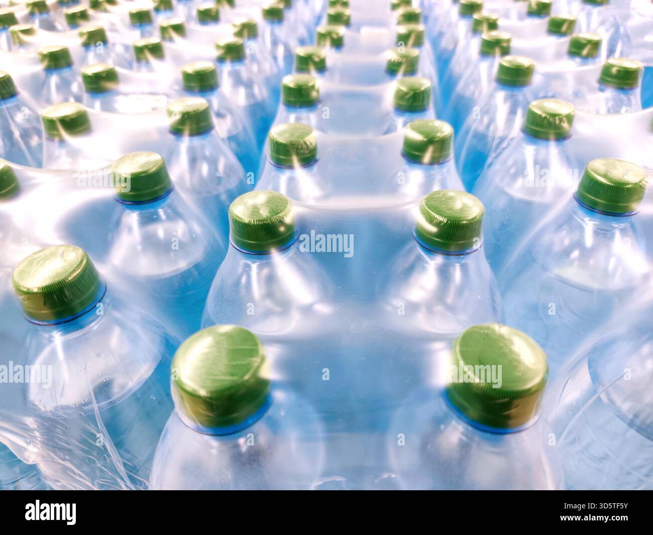 Più bottiglie d'acqua in plastica ermeticamente confezionate in pellicola termoretraibile, viste dall'alto. Tappi verdi, flaconi blu, puliti, visivi freschi, idratazione, massa Foto Stock