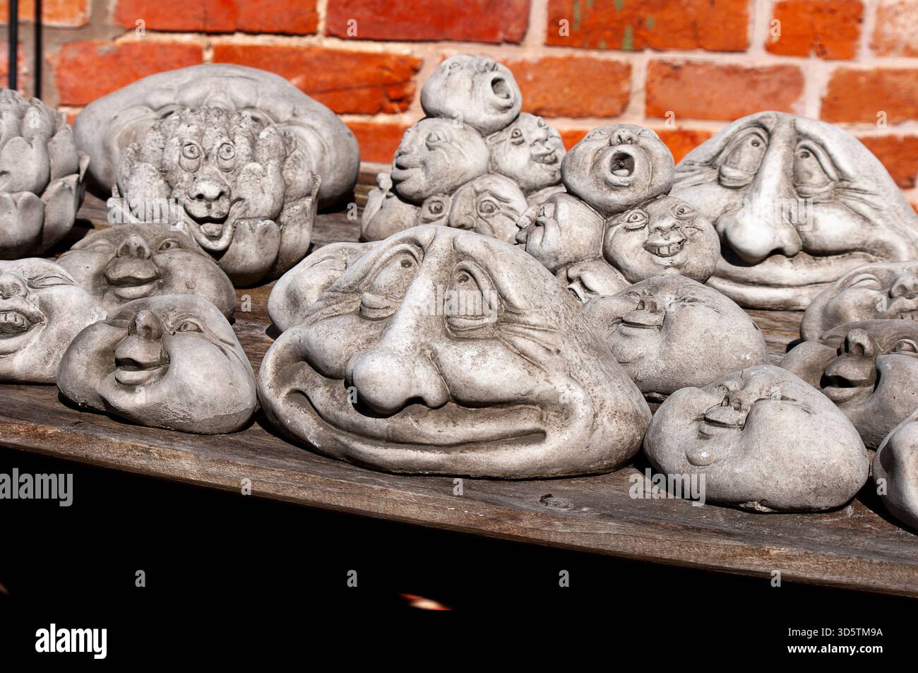 Ornamenti da giardino su una panchina di legno composti da brutti gnomi come teste con volti divertenti che sorridono o ridono. Foto Stock