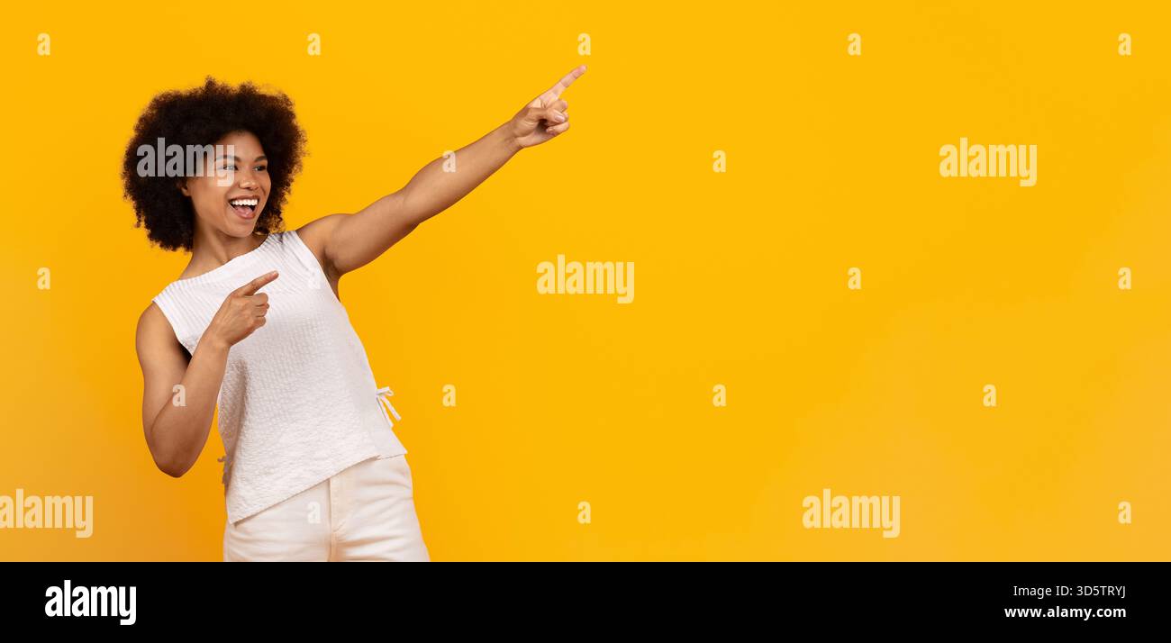 Felice donna afroamericana che punta verso l'alto eccitatamente con espressione gioiosa Foto Stock