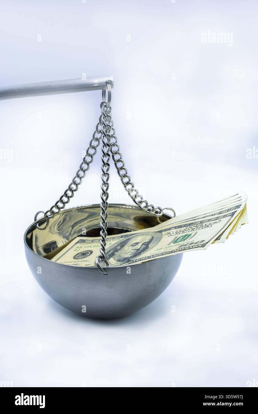Banconote in dollari USA collocate in una ciotola metallica a scala sospesa, simbolo dell'equilibrio finanziario, della giustizia economica, della misurazione della ricchezza e delle decisioni monetarie Foto Stock