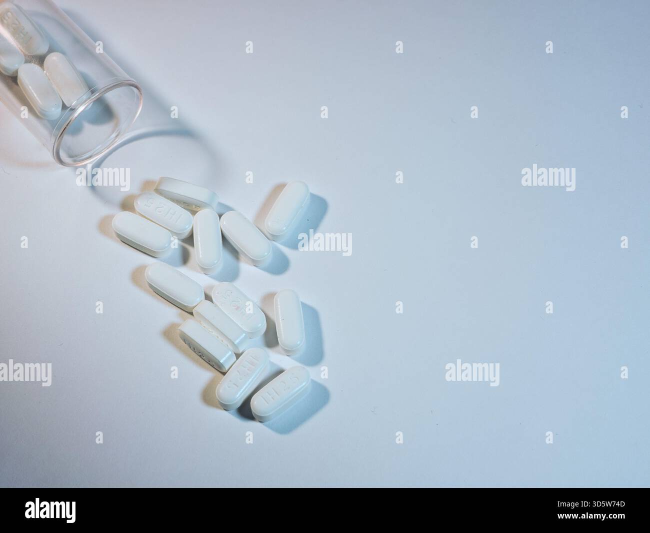Pillole bianche fuoriuscite da flacone trasparente - immagine dall'alto di pillole oblunghe bianche versate da una bottiglia di plastica trasparente su una superficie leggera. Medico, farmacista Foto Stock