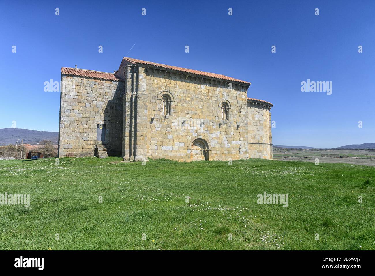Storica chiesa romanica di San Martino a Matalbaniega, Spagna, con mura in pietra e un campanile sotto un cielo azzurro Foto Stock