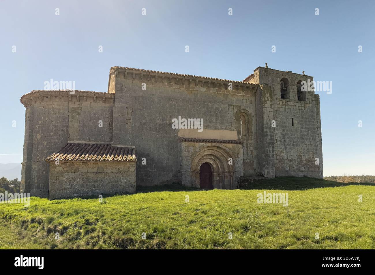 Storica chiesa romanica di San Martino a Matalbaniega, Spagna, con mura in pietra e un campanile sotto un cielo azzurro Foto Stock