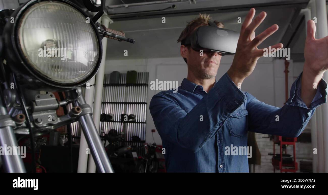 Uomo in piedi in camicia di denim con visore VR che manipola parti virtuali in garage, con fari Foto Stock