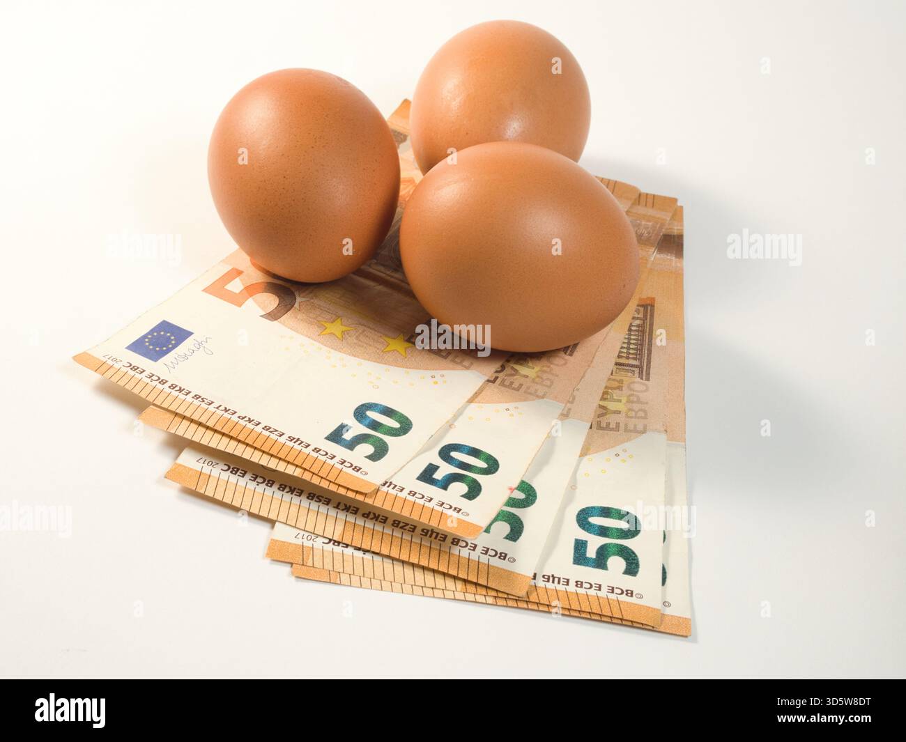 Uova e banconote in euro - tre uova marroni poggiano su una pila di banconote da 50 euro, simboleggiando l'aumento dei costi alimentari, l'inflazione economica e le spese di spesa Foto Stock