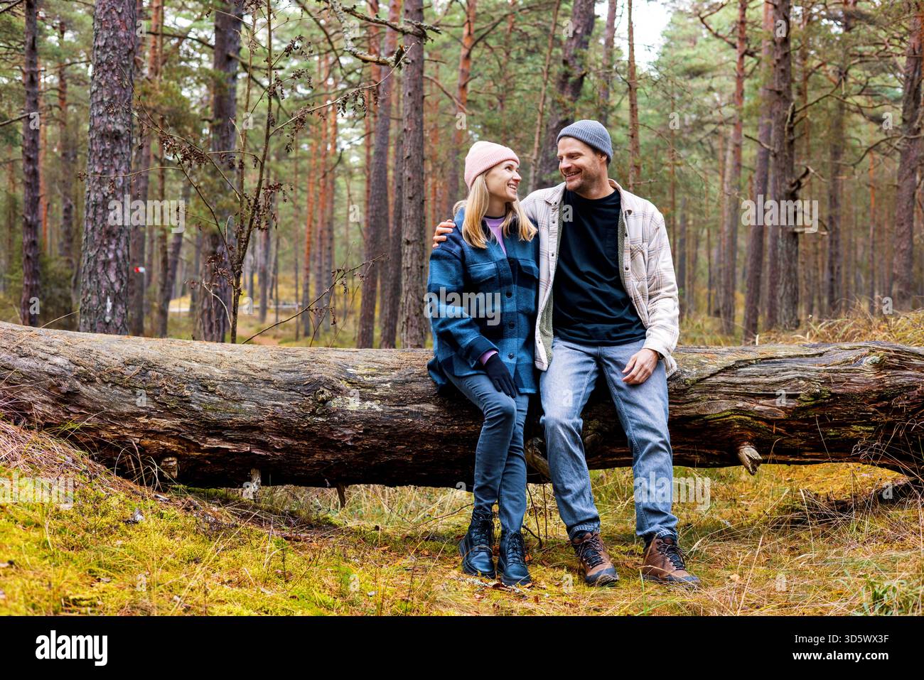 coppia sorridente seduta e riposata sull'albero caduto dopo una passeggiata nel parco autunnale Foto Stock