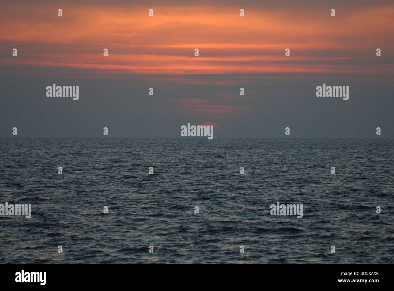 Tramonto sul mare Adriatico con un mezzo sole in rosso e arancione Foto Stock
