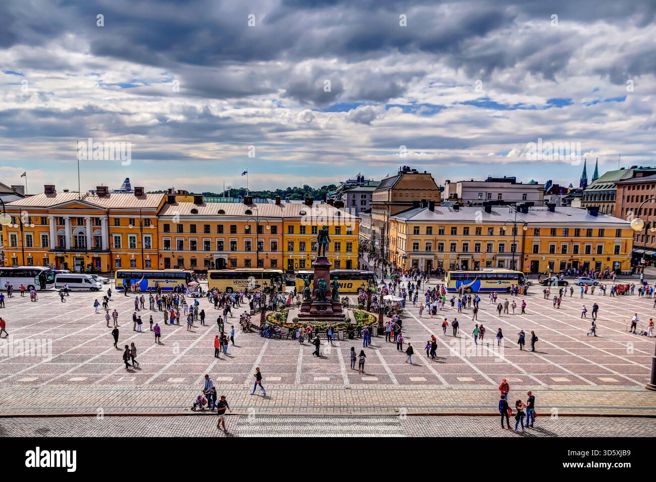Piazza del Senato a Helsinki con folle che camminano attraverso la piazza aperta, incorniciata da storici edifici gialli sotto spettacolari nuvole. Foto Stock