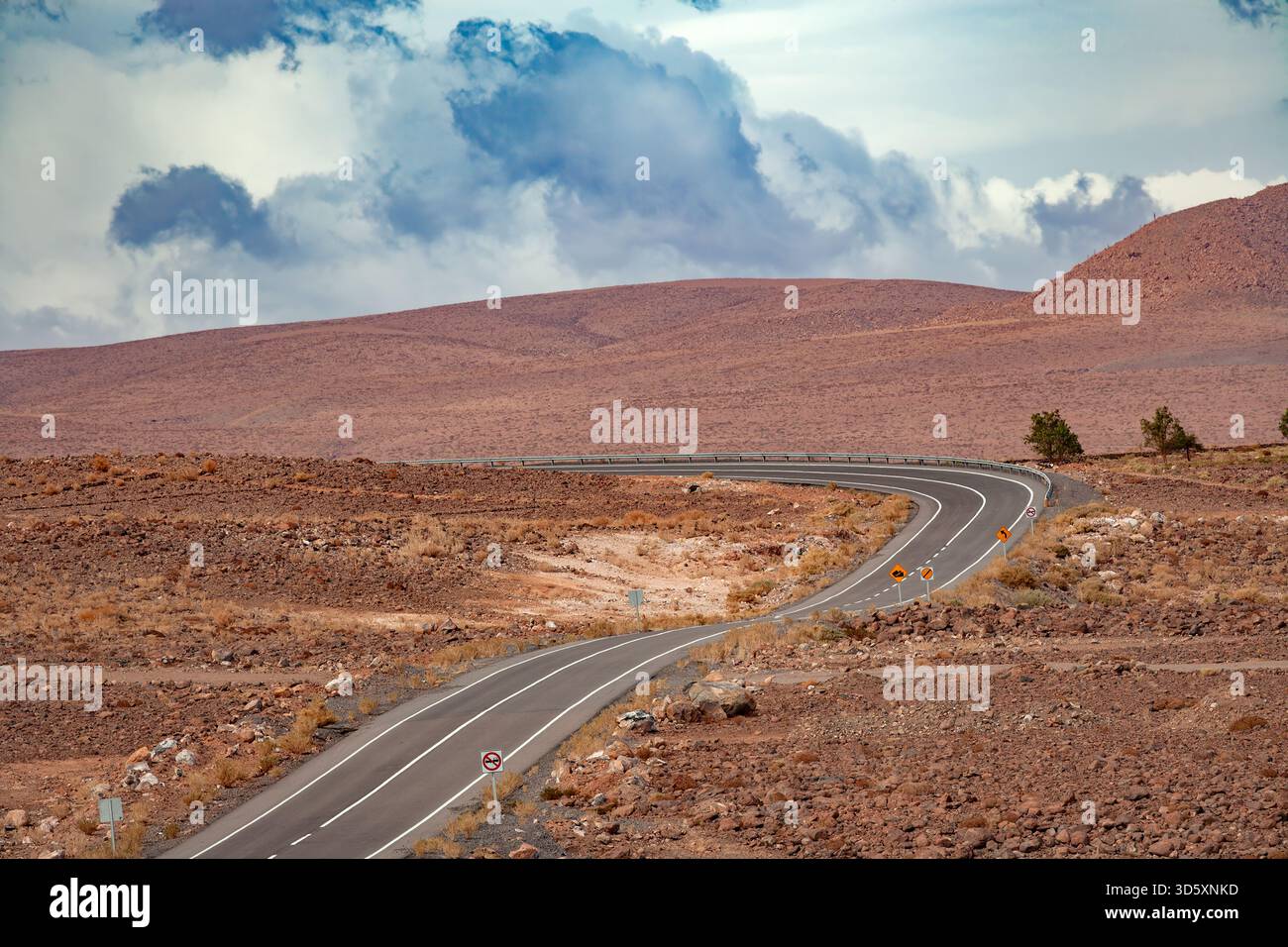 Un'autostrada asfaltata si snoda attraverso il paesaggio desolato e roccioso delle alte pianure del deserto di Atacama vicino a San Pedro de Atacama, in Cile. Foto Stock