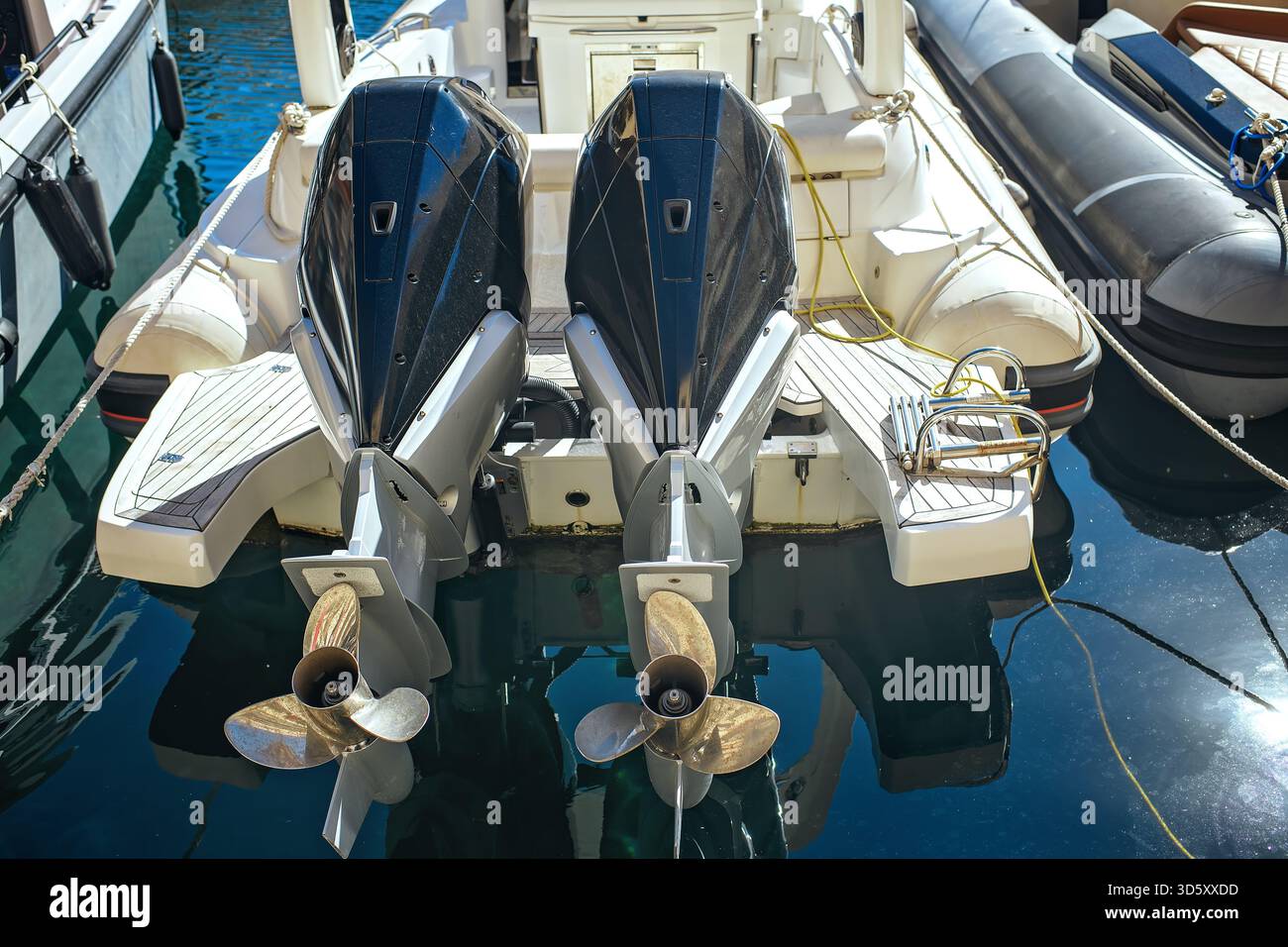 Primo piano di due motori marini fuoribordo su un moderno motoscafo in un porticciolo, con dettagli sul ponte, eliche e riflessi sull'acqua in una giornata di sole. Foto Stock