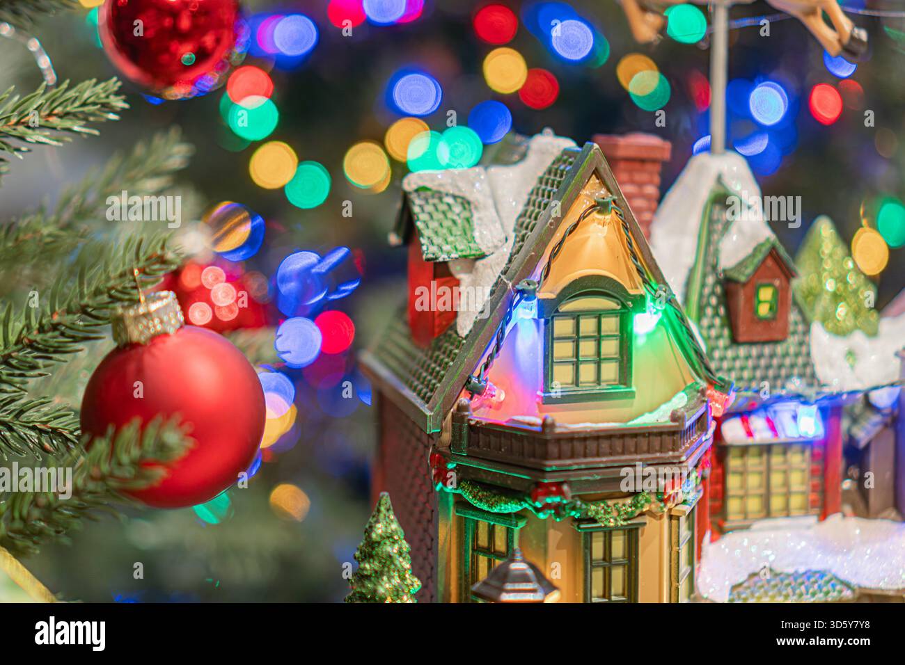Festività natalizie con albero di Natale adornato da luci e ornamenti colorati, tra cui un grande ornamento a forma di casa ambientato sullo sfondo Foto Stock