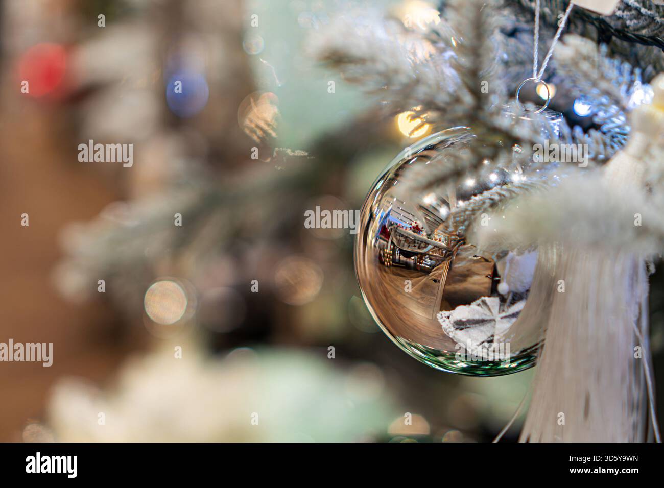 Scena natalizia al coperto con un ornamento sfocato che riflette l'ambiente circostante su un albero, adornato da luci bianche e altre decorazioni, sotto un morbido e caldo labbro Foto Stock