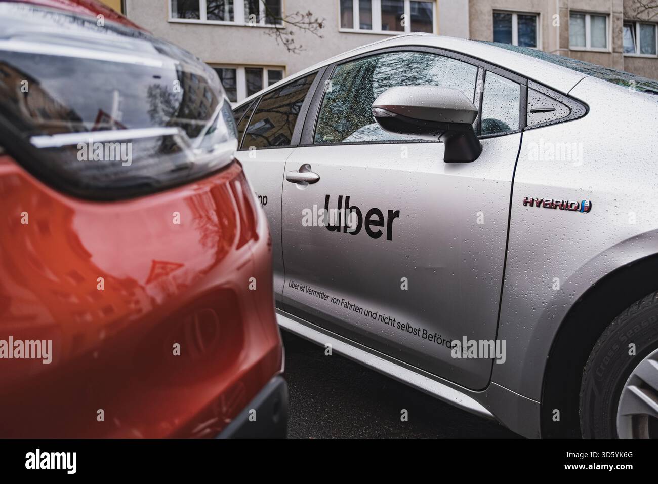 Auto ibrida Silver Uber parcheggiata in una strada cittadina vicino a un veicolo rosso Foto Stock