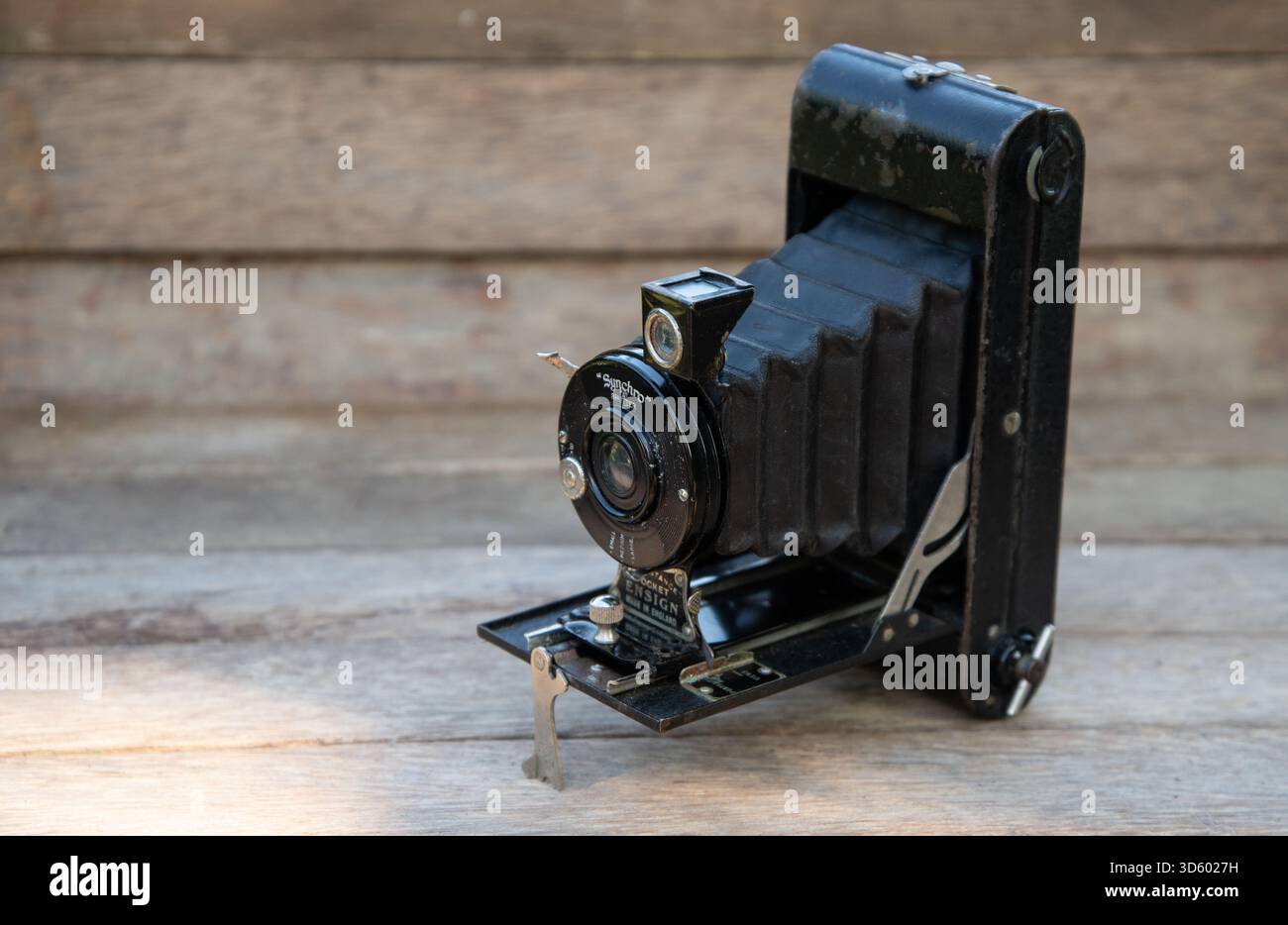 Primo piano di una classica telecamera pieghevole Ensign con soffietto, visualizzata su una superficie rustica in legno. Ideale per temi di storia della fotografia e vintage te Foto Stock