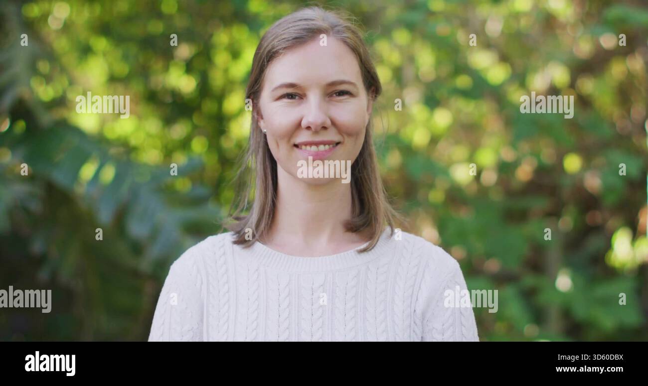 Donna in piedi in mezza età che indossa un maglione bianco in maglia di cavo e piccoli orecchini a bottone in giardino Foto Stock