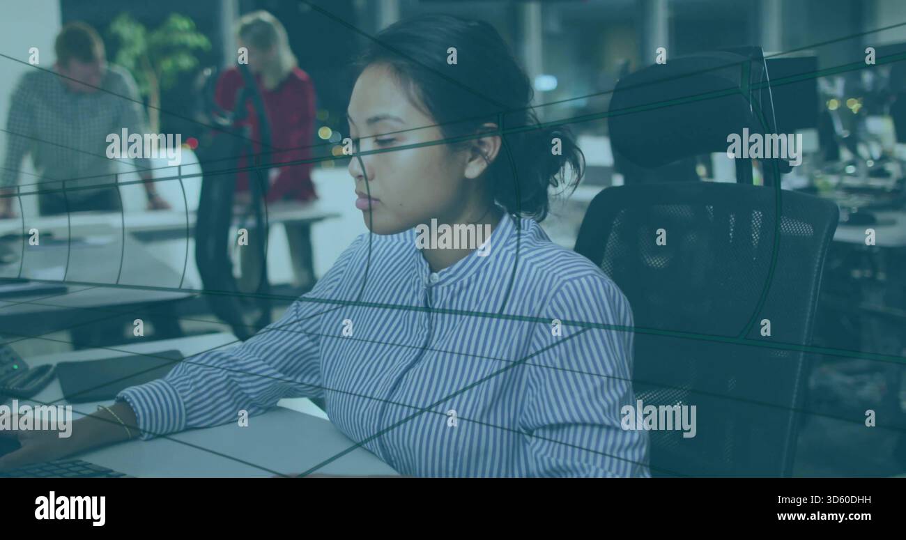 Donna seduta che indossa una blusa a righe in un ufficio open space, con monitor e tastiera Foto Stock