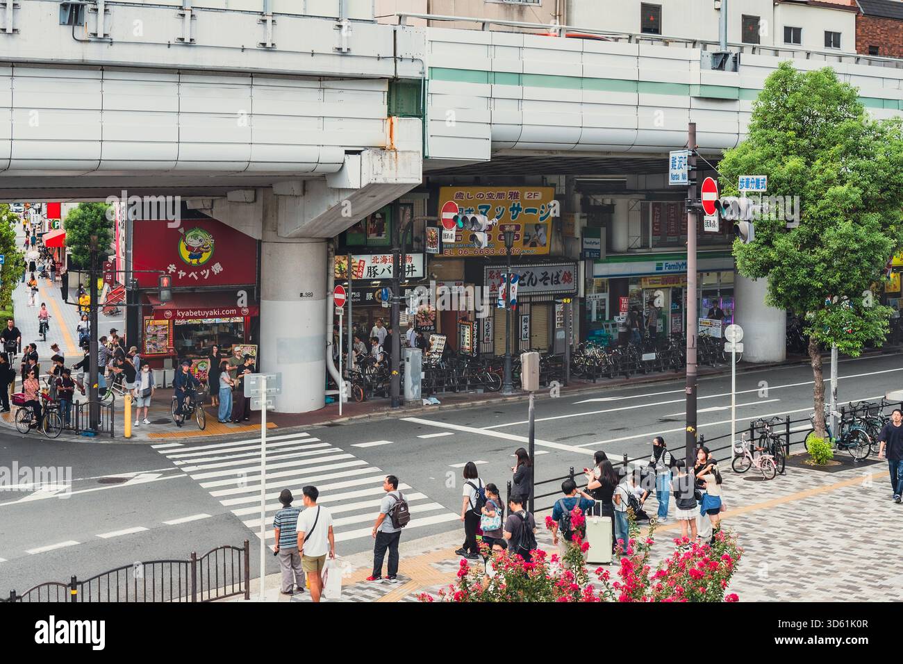 Una vista dall'alto di un trafficato incrocio urbano di Osaka, con pedoni che attraversano la strada sotto un cavalcavia sopraelevato dell'autostrada. Foto Stock