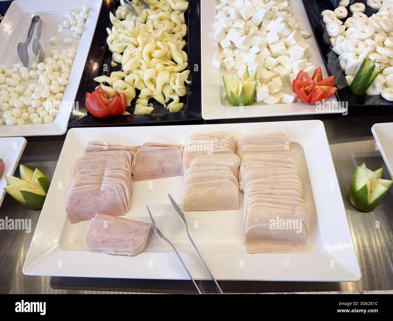 Un tavolo a buffet presenta formaggi assortiti e fette di affettati ordinatamente disposte con decorazioni vegetali Foto Stock