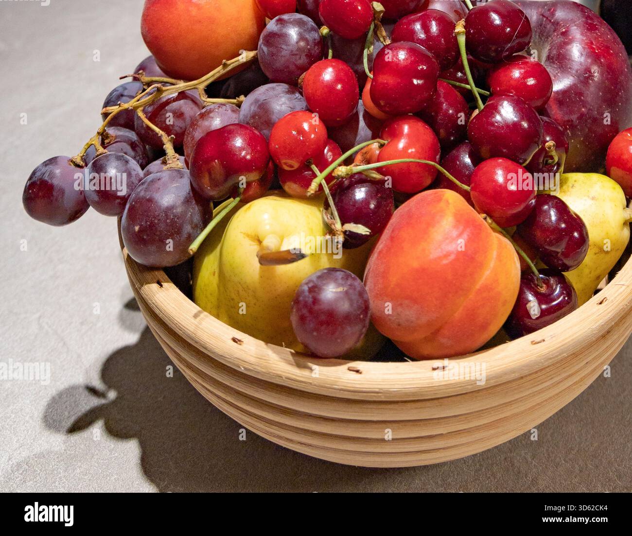 Primo piano di uva fresca e prugne in una ciotola bianca decorativa su un tavolo di legno. La bassa profondità di campo enfatizza il mangiare sano e l'interno Foto Stock