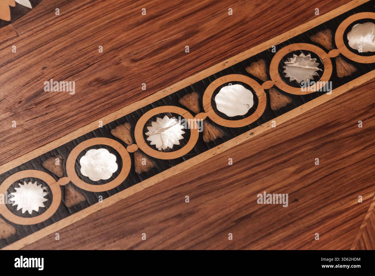 Una vista ravvicinata di un pavimento in parquet con intarsi in legno su una superficie in legno duro lucido. Gli inserti di shell circolari formano un motivo ripetuto lungo una striscia stretta, Foto Stock