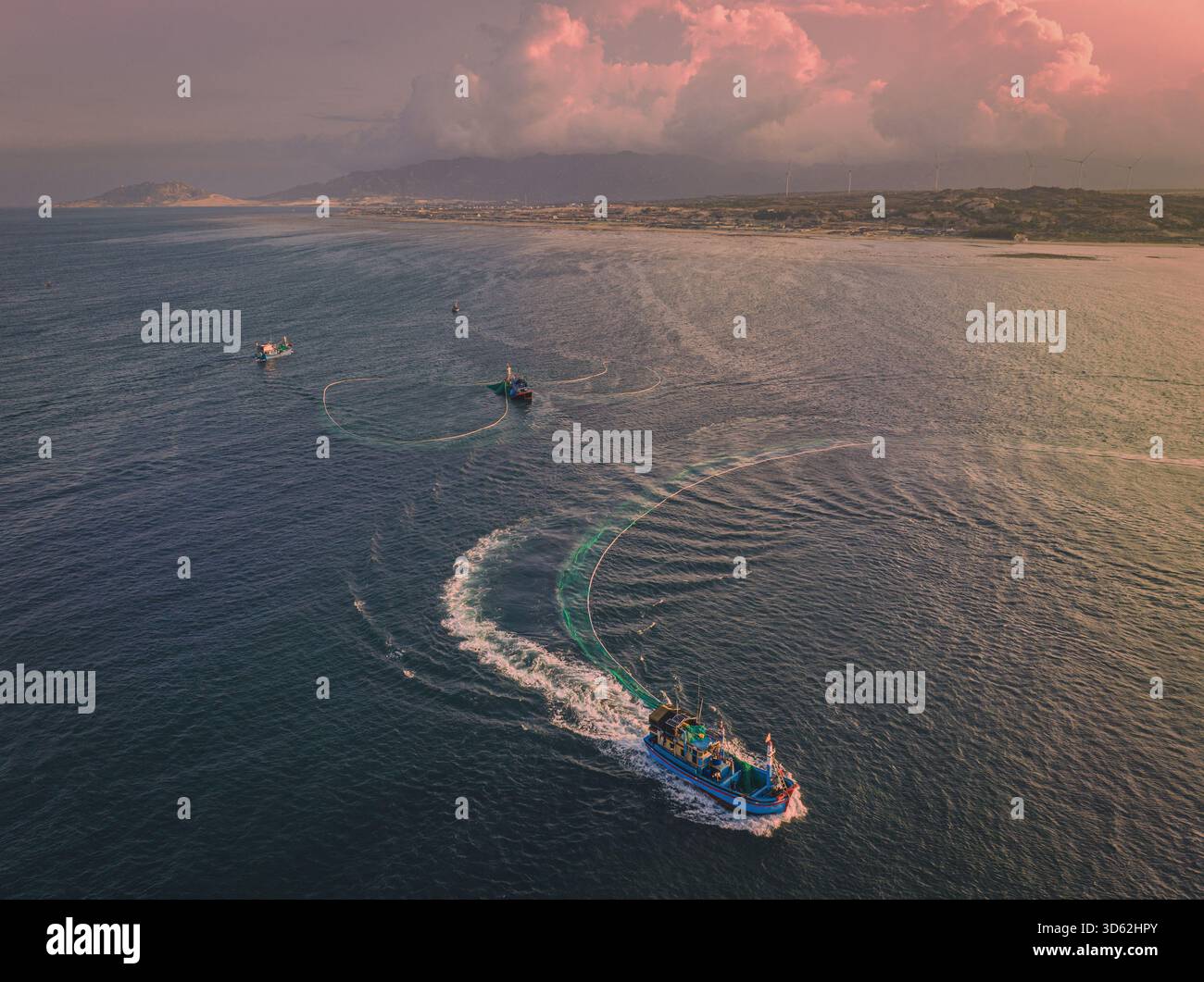 Vista aerea delle barche da pesca che attraversano il mare blu profondo, lasciando vorticosi sentieri sotto un cielo spazzolato di tonalità rosa, Tuy Hoa, Phu Yen, Vietnam. Foto Stock