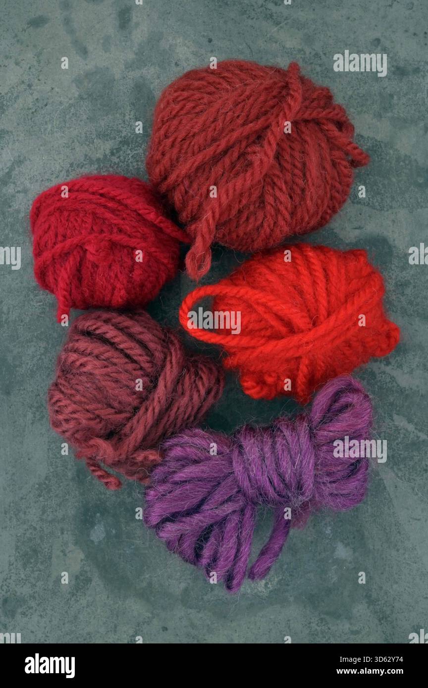 Cinque palline di lana, quattro di loro rossi diversi e una viola Foto Stock