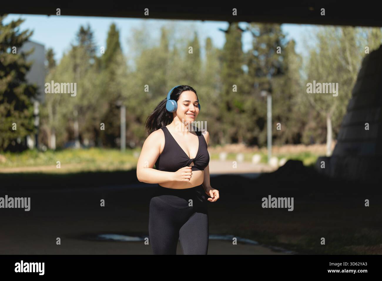 Una giovane donna forte gioca a sport e corre felice nel parco, ascoltando musica con le cuffie Foto Stock