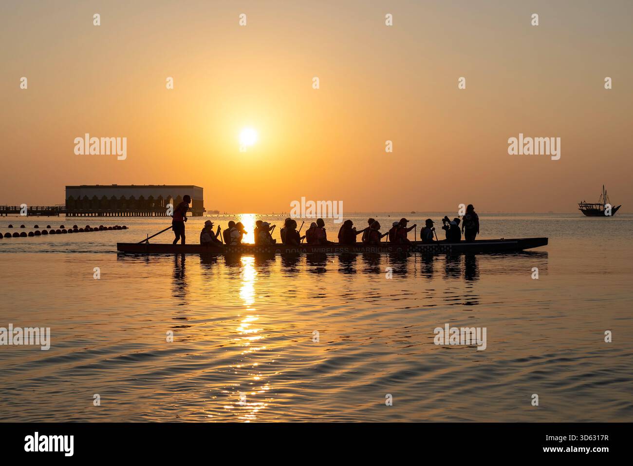 Doha, Qatar - 24 ottobre 2025: Persone silhouette che vogano in barca drago al tramonto al Villaggio culturale di Katara Foto Stock