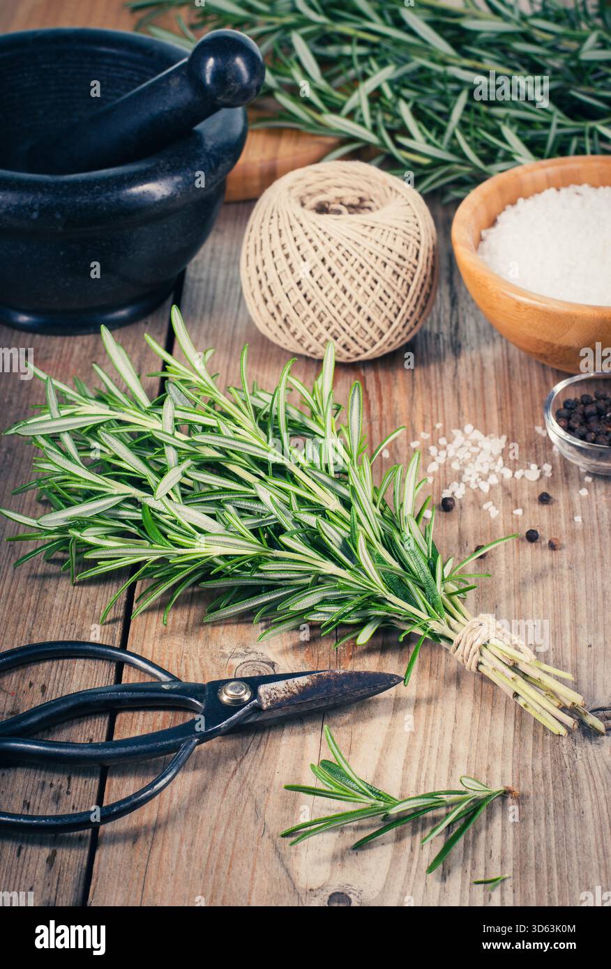 Rosmarino fresco aromatico con sale marino grezzo e grani di pepe nero su una tavola rustica di legno. Perfetto per temi culinari, alimentazione sana, Mediterraneo Foto Stock