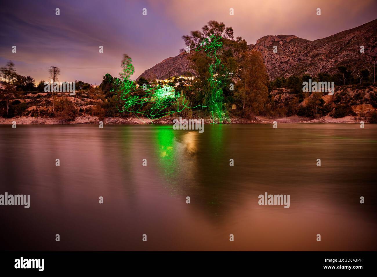 Una dinamica fotografia notturna del bacino idrico Amadorio, che combina lunga esposizione con la pittura a luce. Striature di luce verde brillante tracciati Foto Stock