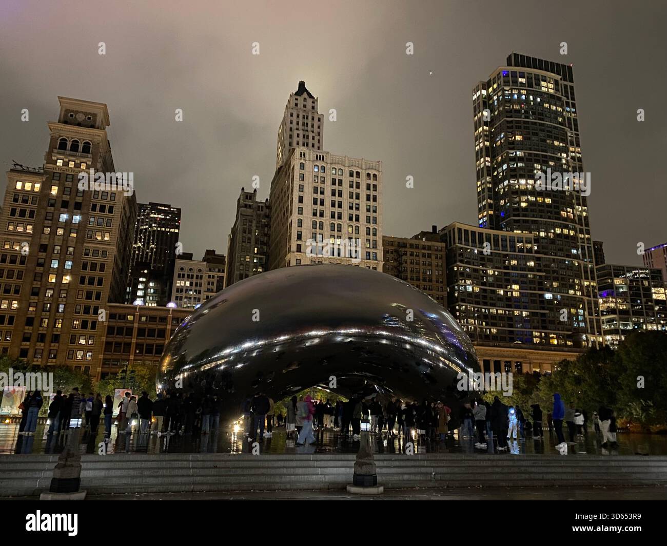 Paesaggio urbano notturno editoriale caratterizzato da una scultura pubblica riflettente ambientata contro grattacieli illuminati nel centro di Chicago. Nov. 2025. Dopo la pioggia. - Immagine stock catturata con smartphone