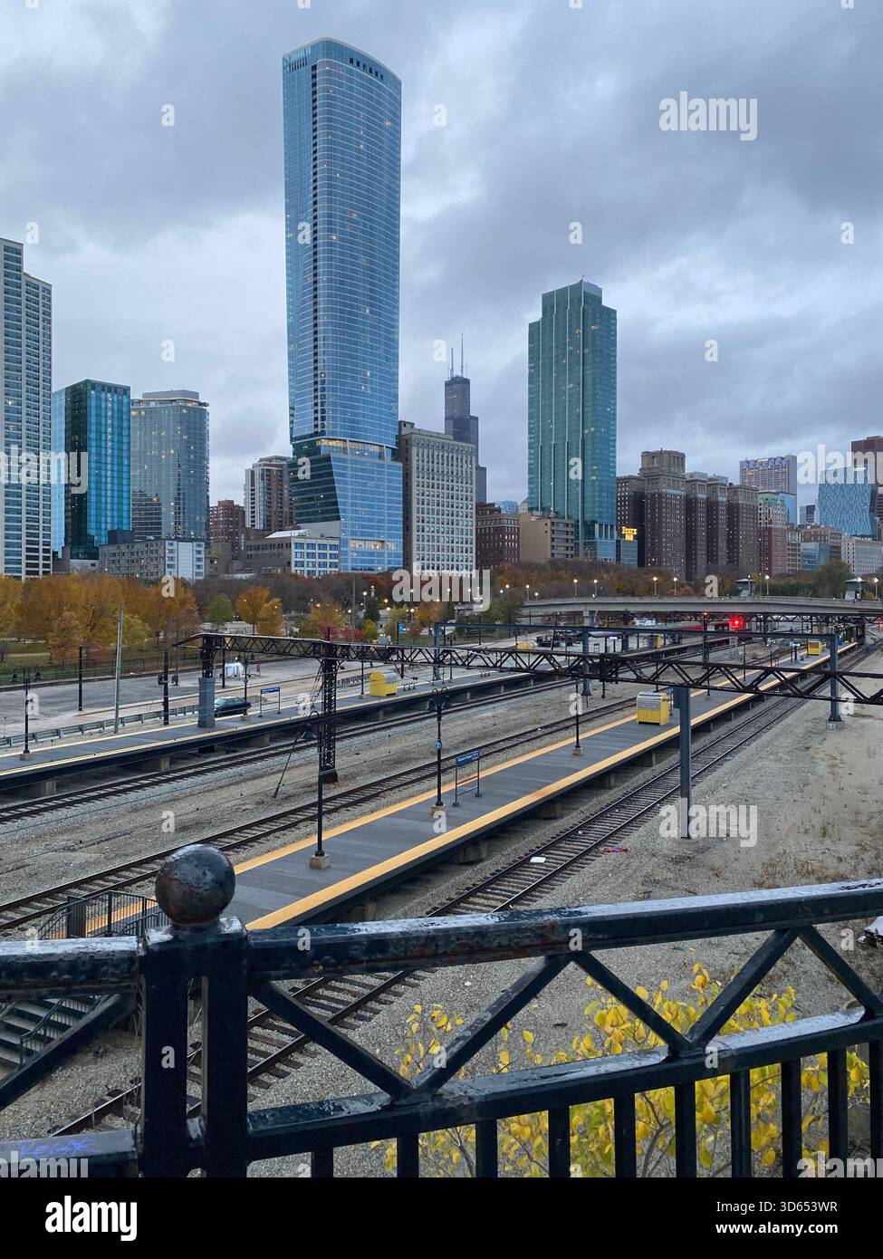 Diversi binari ferroviari che si estendono verso uno skyline del centro, pieno di grattacieli moderni e alti. Cielo coperto e colori autunnali attenuati. - Immagine stock catturata con smartphone