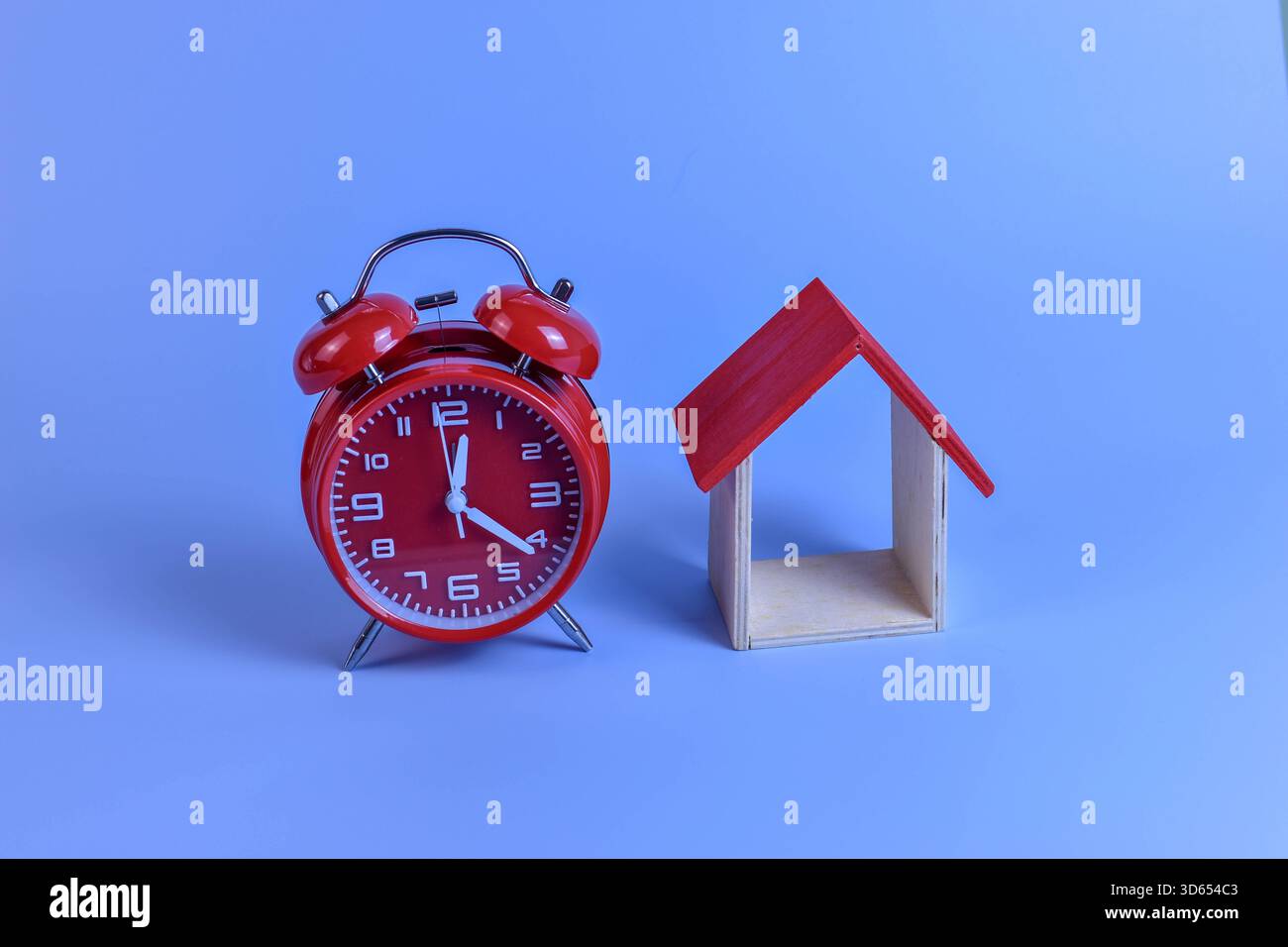Sveglia rossa e modello minimale di casa su sfondo blu evocano temi del tempo, della vita domestica e della semplicità strutturata. Foto Stock