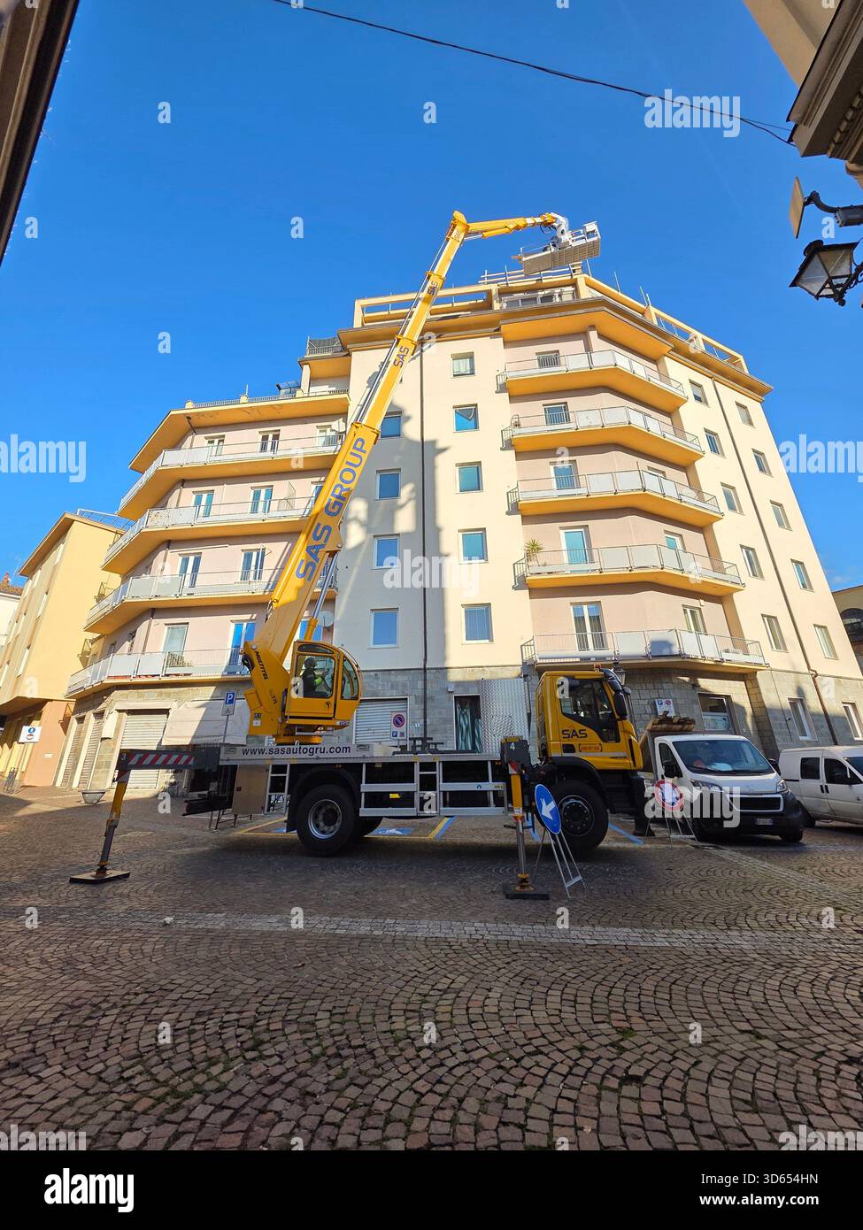 Piattaforma di lavoro aerea gialla che raggiunge un alto edificio per manutenzione in una strada cittadina. "Pianta gialla in via cittadina per manutenzione grat - Immagine stock catturata con smartphone