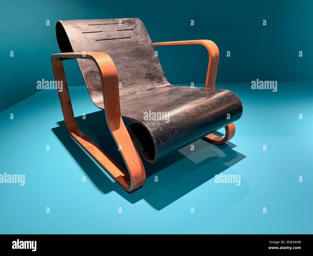 Poltrona modernista vintage Paimio Chair di Alvar Aalto con telaio in compensato curvo e seduta nera su sfondo turchese Foto Stock