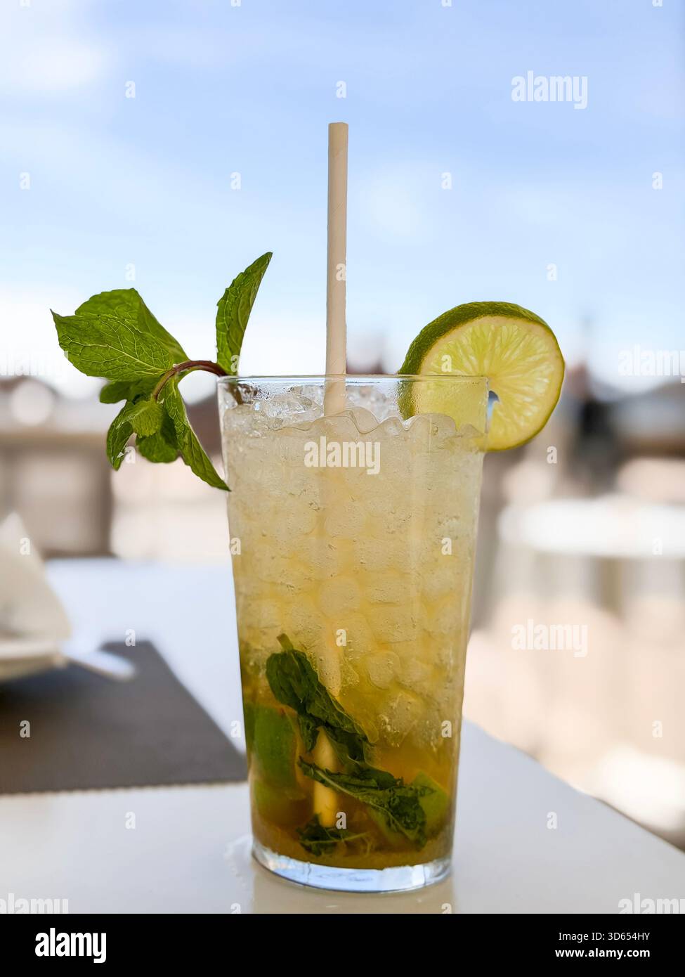 Cocktail di mojito ghiacciato servito in un bicchiere alto con foglie di menta, ghiaccio tritato, fetta di lime e paglia di carta su un tavolo da caffè all'aperto mallorca spagna Foto Stock