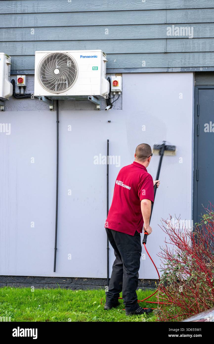 lavavetri e operaio addetto alla manutenzione delle proprietà utilizzando una spazzola a manico lungo per pulire i lati di un locale commerciale. Detergente commerciale con spazzola. Foto Stock