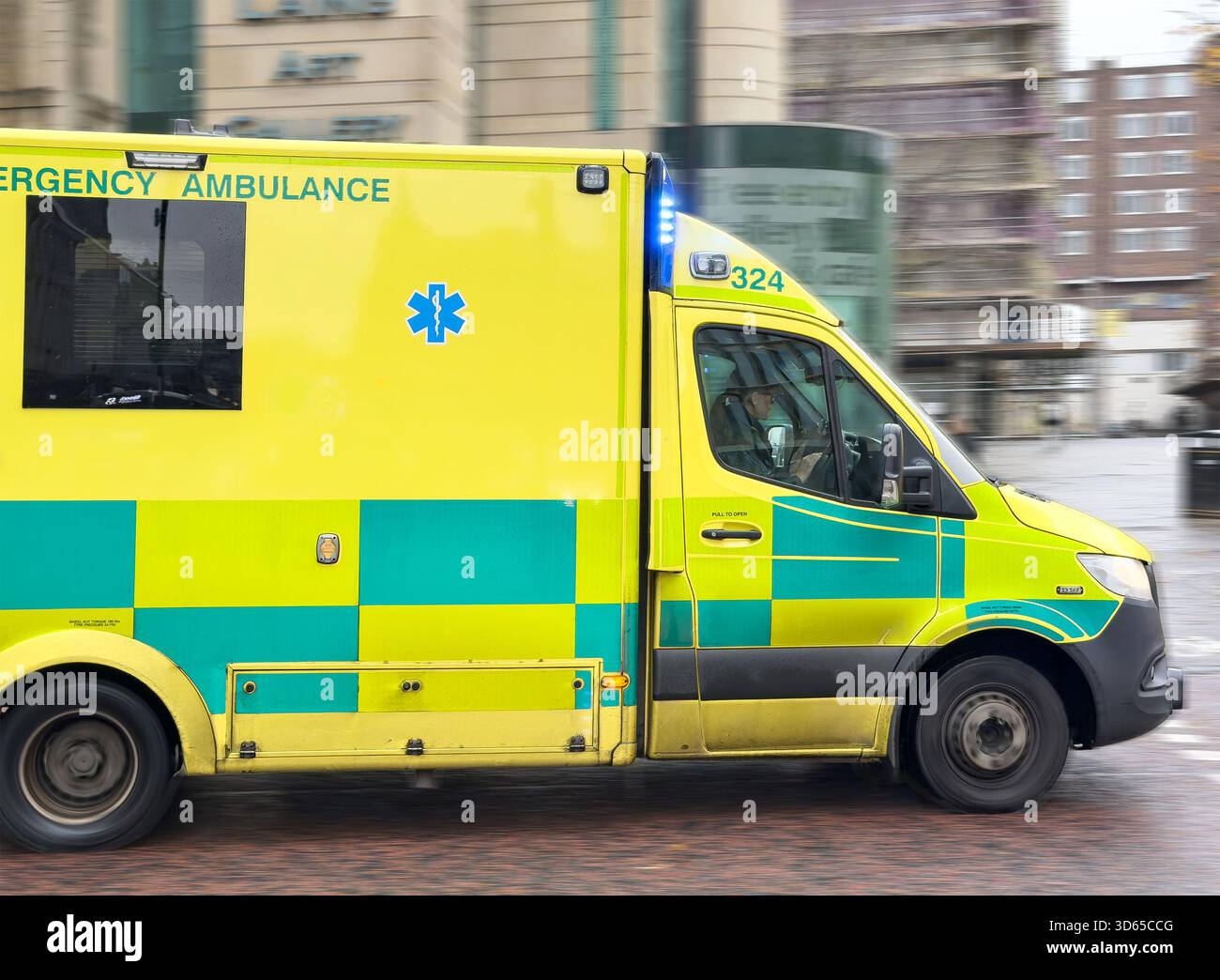 Ambulanza di emergenza del Regno Unito in movimento nell'area urbana di newcastle upon tyne con alberi sfocati ed edifici sullo sfondo - Immagine stock catturata con smartphone