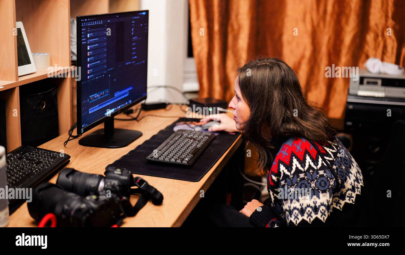 Donna concentrata che lavora all'editing di video e foto alla scrivania da casa con monitor per computer e fotocamere professionali: Un concetto moderno di lavoro remoto Foto Stock