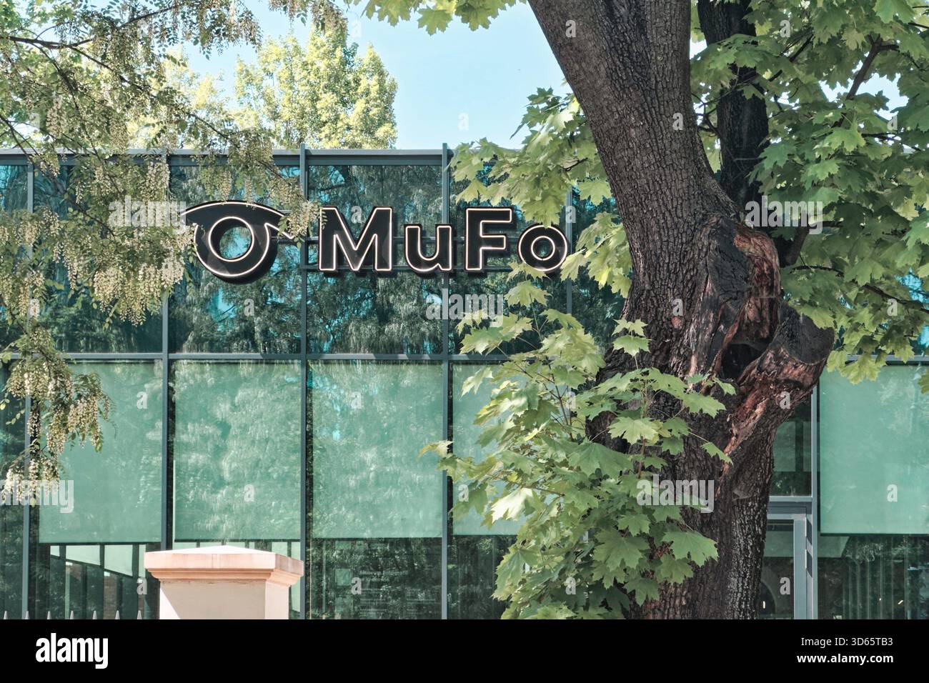 Esterno del MuFo Museum of Photography di Kraków, Polonia, parzialmente nascosto dietro alberi verdi e facciata in vetro. Foto Stock