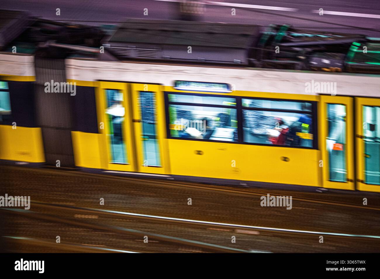 Un tram giallo si muove senza intoppi attraverso le vivaci strade di Berlino di notte. Le luci della città illuminano la scena, mostrando i passeggeri all'interno. Foto Stock