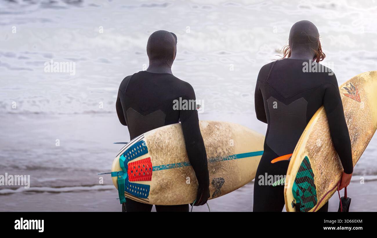 Druridge Bay, Northumberland 18 ottobre 2025 - coppia di surfisti, surf nella Baia di Druridge durante un'ondata autunnale. Foto Stock