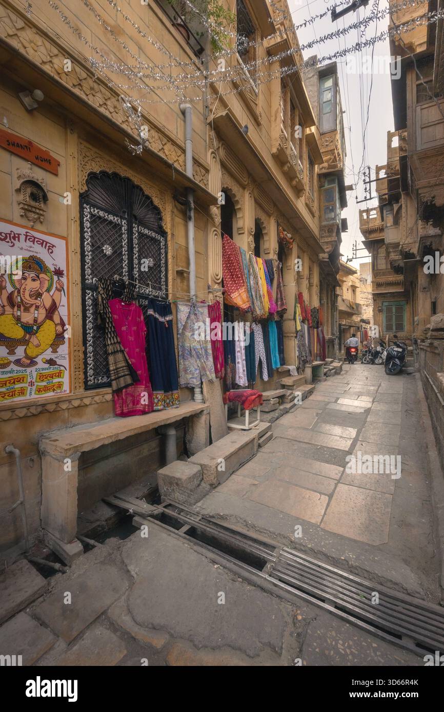 Abbigliamento tradizionale e tessuti colorati esposti lungo uno stretto vicolo lastricato di pietra all'interno del forte Jaisalmer, Rajasthan, che mostra l'artigianato locale. Foto Stock