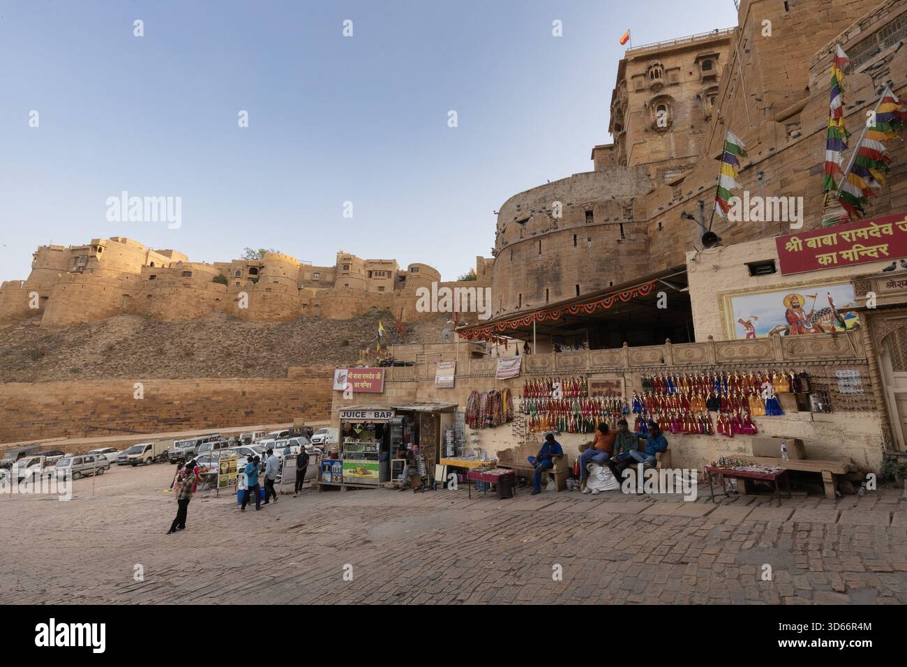 Venditori e piccoli negozi alla base del forte di Jaisalmer, con bastioni di arenaria dorata e attività serali intorno al monumento storico. Foto Stock