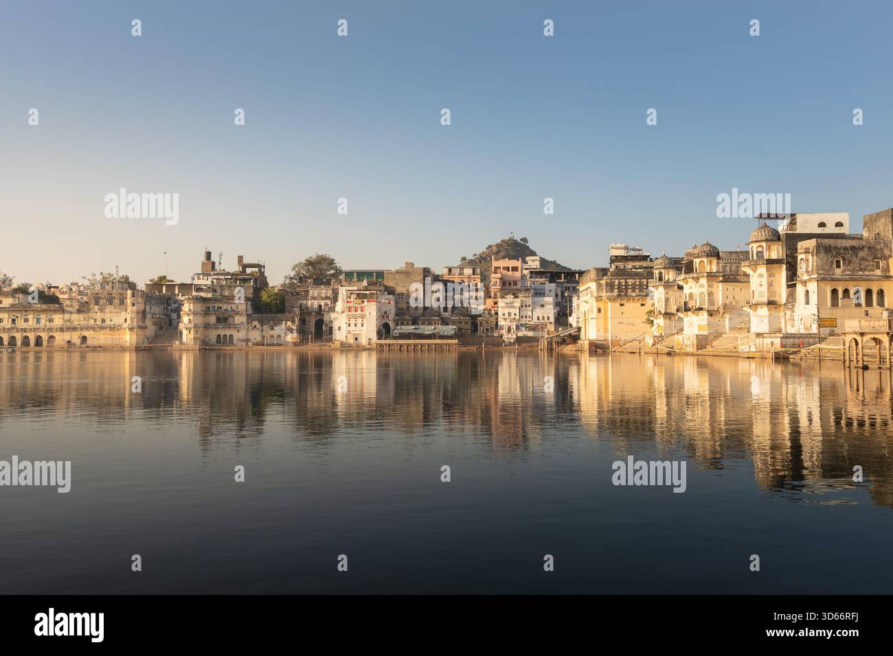Vista mattutina dei Ghati di Pushkar riflessa nelle calme acque del lago, con templi storici e case che brillano nella luce calda e soffusa dell'alba presto. Foto Stock